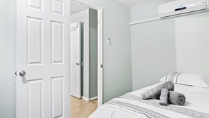 A bedroom with a bed, a white door, a wall-mounted air conditioner, and a hallway.