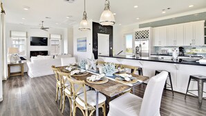 A spacious living area with a dining table set for six, surrounded by white furniture.