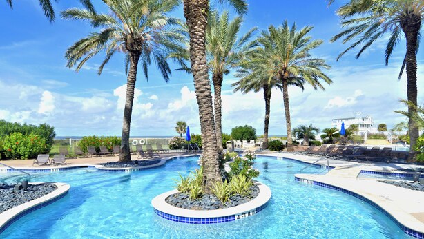 A swimming pool with a circular island, palm trees, and lounge chairs.