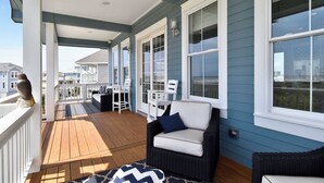 A covered porch with a wooden deck, white railings, and a seating area with a wicker chair and a small table.