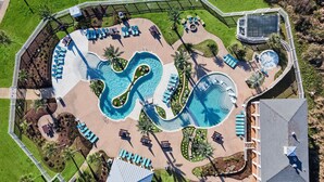 An aerial view of a resort with a large pool, sun loungers, and a small building. - Wine Down by Ryson Vacation Rentals (Galveston)