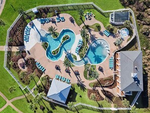 An aerial view of a resort with a large pool, sun loungers, and a small building. - Wine Down by Ryson Vacation Rentals (Galveston)
