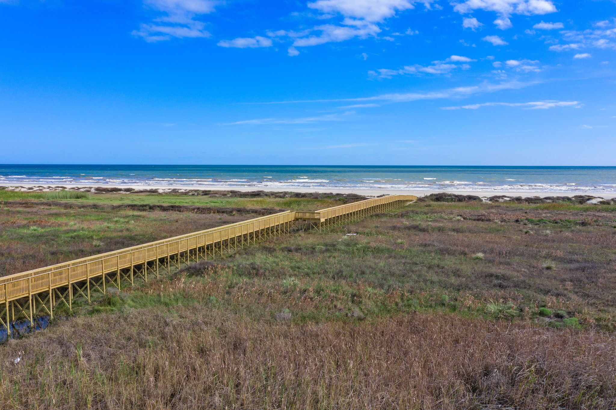 Une promenade en bois qui mène à une plage, avec un ciel dégagé.