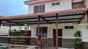 Ein überdachter Patio-Bereich mit gefliestem Boden, Topfpflanzen und einer Sitzecke mit Stühlen und einem Tisch.