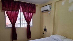 Ein Schlafzimmer mit Bett, einem Fenster mit Vorhängen, einer Klimaanlage und einer Steckdose.