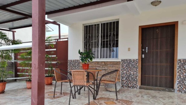Eine überdachte Terrasse mit Tisch, Stühlen, einer Topfpflanze und einer Tür mit der Nummer 5.