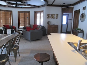 A spacious living area with a large sofa, a dining table with chairs, and a kitchen area with a sink.