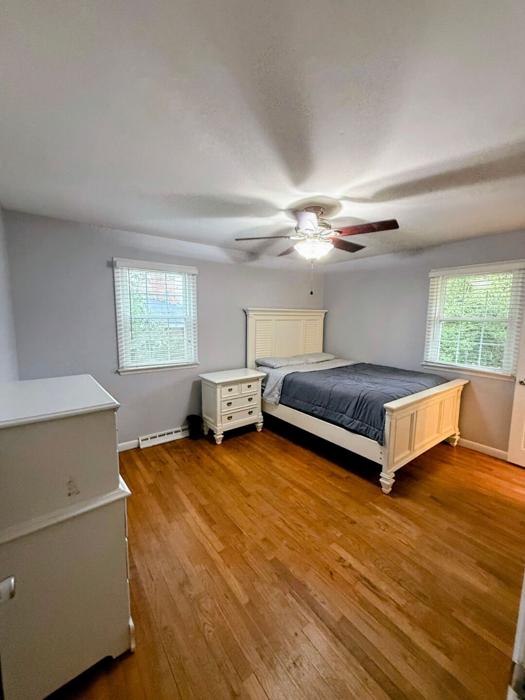 Un dormitorio con cama, mesitas de noche, cómoda y ventilador de techo.