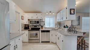 A modern kitchen with white cabinets, a built-in microwave, oven, and dishwasher. There is a granite countertop and a window with blinds. - 3 Bed, 2 Bath Cabin in Munds Park AZ Close To Flagstaff and Sedona (Munds Park)