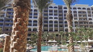 Un hotel con piscina, palmeras y varios balcones.