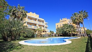 Un edificio residencial con piscina rodeado de palmeras y césped.