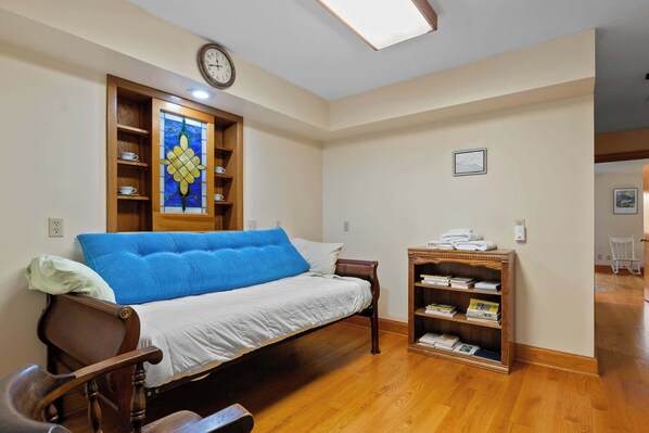 A bedroom with a bed, a wooden side table, a bookshelf, a stained glass window, and a clock on the wall.