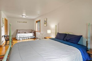 Ein Schlafzimmer mit einem großen Bett, einem kleinen Sofa, einem Sessel, einem Nachttisch mit Lampe und einem Fenster.