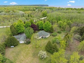 An aerial view of a residential area with two houses, surrounded by dense greenery and a clear sky. - 5 Acres in Ellison Bay! The Goddess Door Family Home (Ellison Bay)