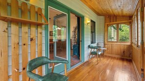A wooden cabin with a porch, a door leading to an interior room, and a window with a view of greenery. - 5 Acres in Ellison Bay! The Goddess Door Family Home (Ellison Bay)