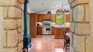 A kitchen with wooden cabinets, a stove, and a window with a view of greenery. - 5 Acres in Ellison Bay! The Goddess Door Family Home (Ellison Bay)