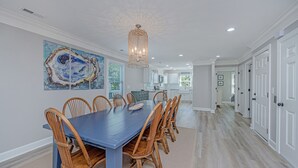 A dining area with a long table and chairs, a chandelier, and artwork on the wall. - DEEP WATER Newly Renovated Waterfront Home-Wren's Nest (Edisto Island)