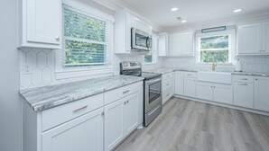 A modern kitchen with white cabinetry, a stainless steel range, and a window with a view of greenery. - DEEP WATER Newly Renovated Waterfront Home-Wren's Nest (Edisto Island)