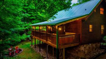 A wooden cabin with a balcony, surrounded by dense forest.