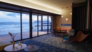 Una habitación moderna con amplios ventanales con vistas al mar, una terraza de madera y un rincón de descanso acogedor con una mesa y sillas.