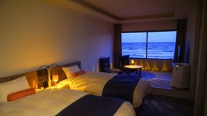 Habitación de hotel con dos camas, vista al océano, una mesita con lámpara y un cesto de basura.