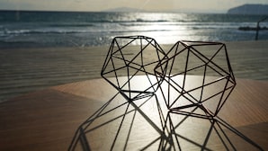 Dos esculturas geométricas sobre una mesa de madera con vistas al océano y montañas distantes.