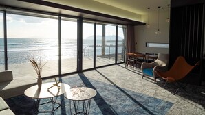 Una habitación de hotel moderna con un balcón grande, un comedor y un espacio de descanso con vistas al mar.