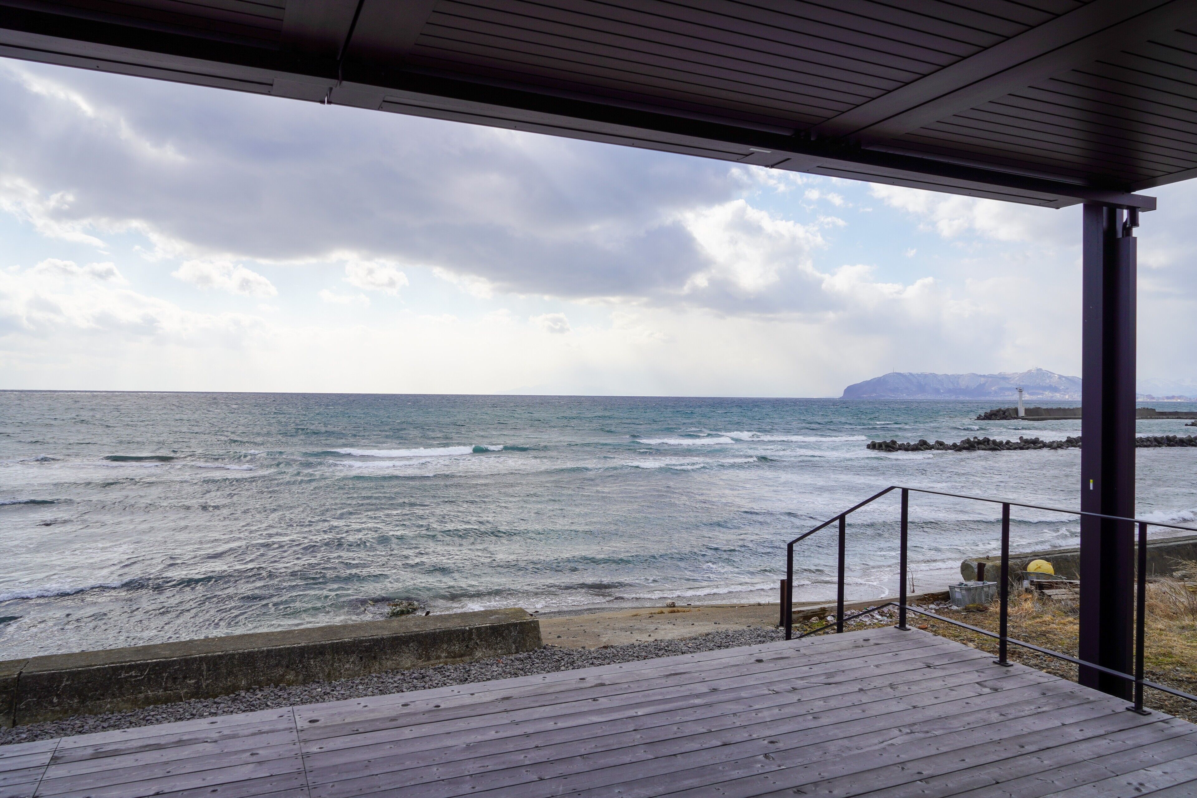 A wooden deck with a railing overlooking a rocky shoreline and the ocean.
