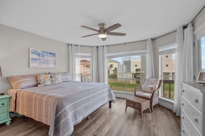 Une chambre avec un grand lit, un ventilateur de plafond, une chaise et une vue sur l’extérieur.