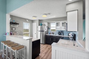 A modern kitchen with a central island, a refrigerator, and a coffee maker.