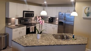 A modern kitchen with granite countertops, stainless steel appliances, white cabinetry, and pendant lighting. - Grand Panama Resort beautiful condo (Panama City Beach)
