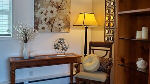 A room with a wooden chair, a lamp, a cabinet, and a floral painting on the wall.