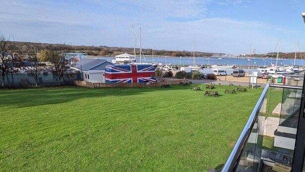 A grassy area with a flag, a marina with boats, and a building with a balcony. - Folly View -  First floor apartment that sleeps 4 guests  in 2 bedrooms (Binfield)
