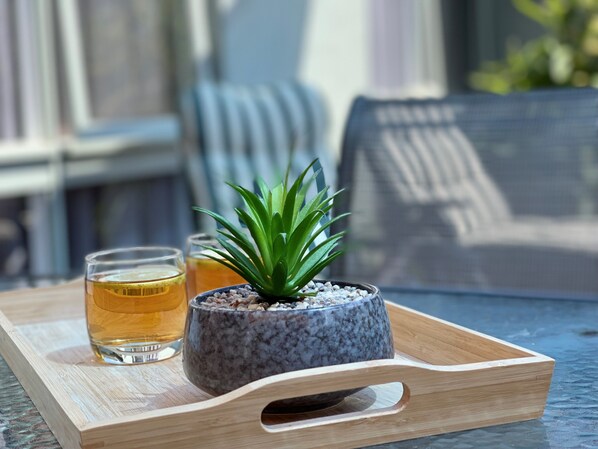 Una pequeña planta en maceta sobre una bandeja de madera, con dos vasos de líquido ámbar, probablemente té, sobre una mesa.