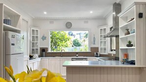 Una cocina moderna con armarios blancos, una isla central y un amplio ventanal con vista a zonas verdes.