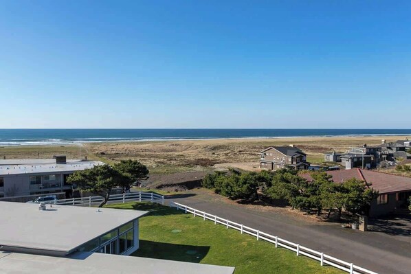 A coastal property with a view of the beach, a fenced driveway, and a modern building with a flat roof.