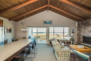 A spacious living area with a high ceiling, a long dining table, a sofa, and a fireplace.