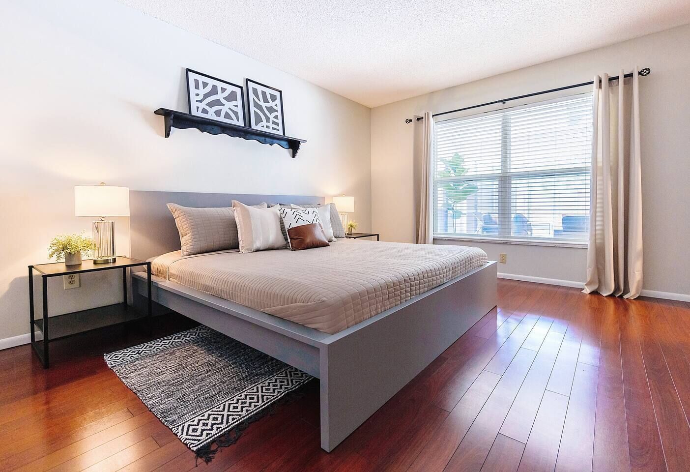 A bedroom with a bed, bedside tables, a rug, a window with curtains, and wall art.