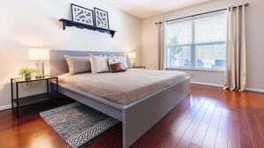 A bedroom with a bed, bedside tables, a rug, a window with curtains, and wall art.