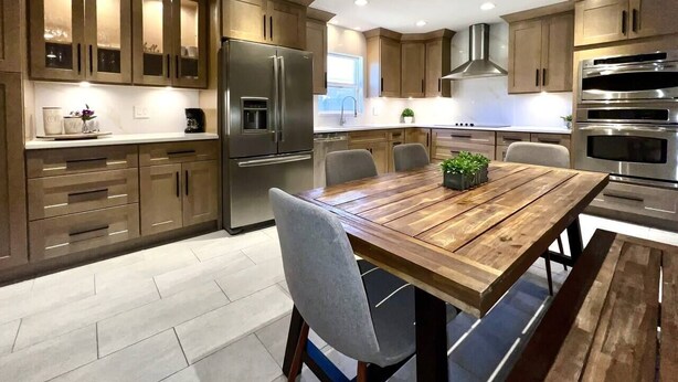A modern kitchen with wooden cabinets, stainless steel appliances, and a wooden dining table with chairs.