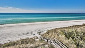 A beach with a wooden boardwalk leading to the shoreline, clear turquoise water, and a sandy beach.