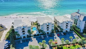 A beachfront hotel with multiple buildings, a parking lot, and a beach in the background.