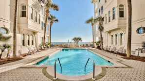 A pool area with a clear view of the ocean, surrounded by palm trees and lounge chairs.