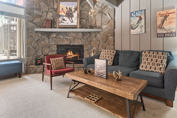 A cozy living room with a stone fireplace, a blue sofa, a red chair, and a wooden coffee table.