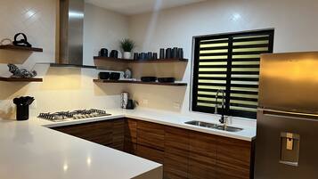Une cuisine moderne dotée d’un îlot central, de meubles de rangement en bois intégrés, d’une hotte en acier inoxydable et d’une fenêtre avec stores.