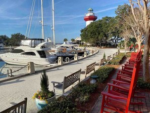 A marina with boats docked, a lighthouse in the background, and a row of red benches along the walkway.