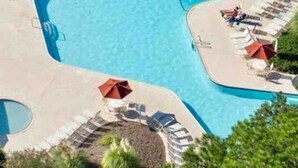 En vy från ovan av en swimmingpool med flera sektioner, omgiven av solstolar och parasoller.
