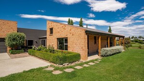 A modern brick house with a covered porch, a well-maintained lawn, and a clear blue sky. - Edgewater Escape - Cromwell Holiday Home (Cromwell)