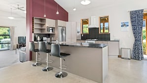 A modern kitchen with a central island, bar stools, and a dining area with a TV. - Edgewater Escape - Cromwell Holiday Home (Cromwell)