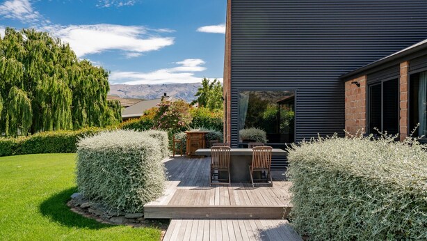 A modern house with a deck, a patio with chairs, and a view of mountains. - Edgewater Escape - Cromwell Holiday Home (Cromwell)